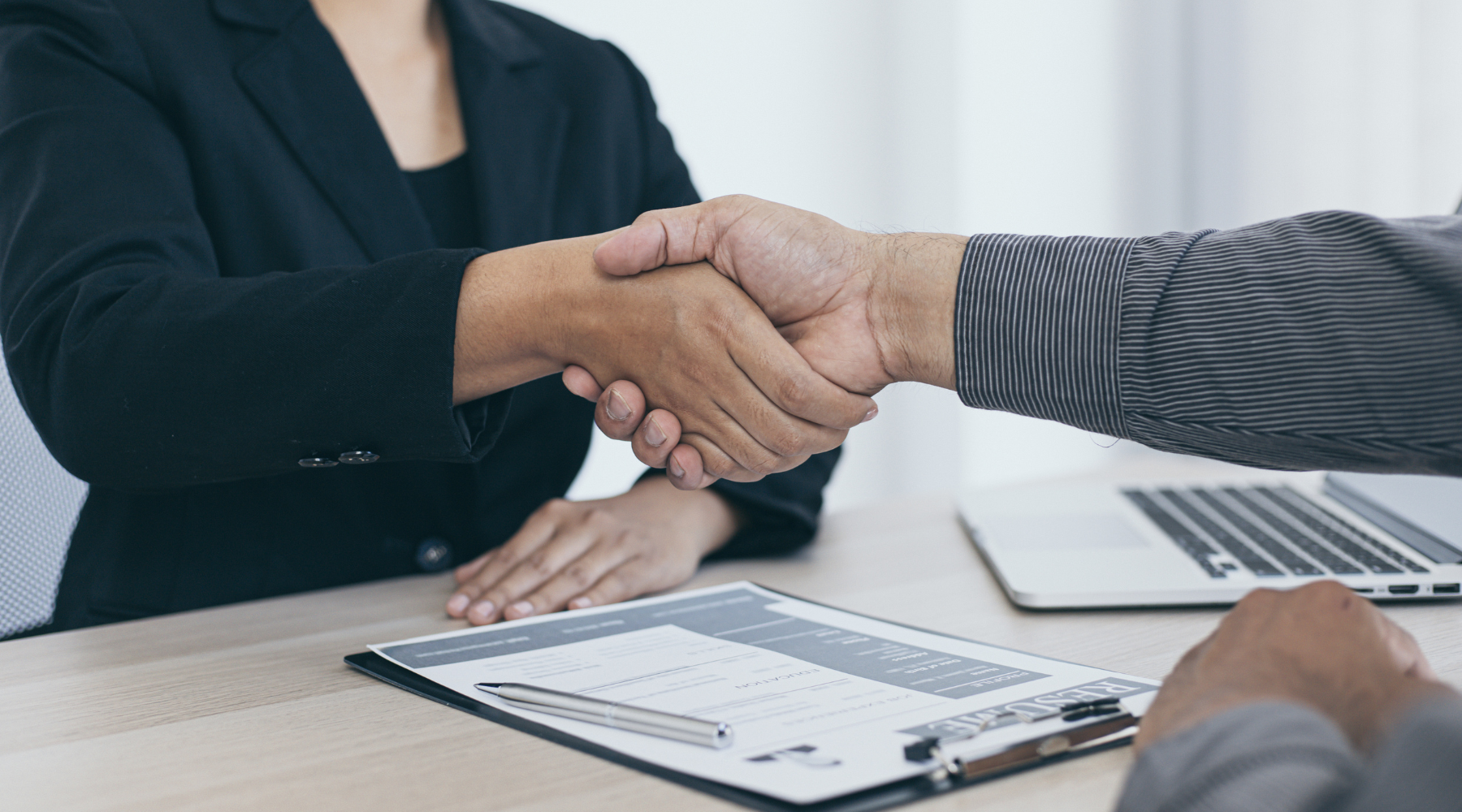 Article cover image for 'the secret to a standout director resume', showing two people on either side of a desk shaking hands