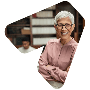 A teacher stands smiling broadly with crossed arms in a library