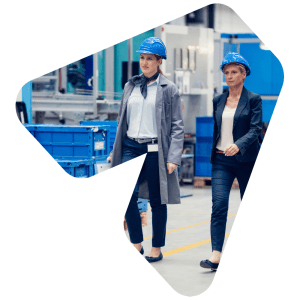 Two well-dressed women in hard hats walk through a manufacturing facility